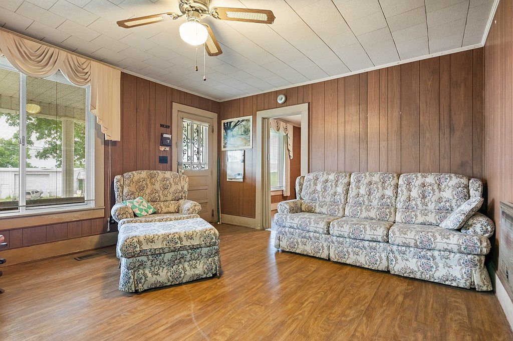 Interior living room of the farmhouse with knotty pine wall paneling, a vintage ceiling fan, and a floral upholstered sofa and chair set