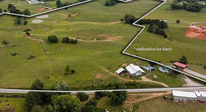 Closer aerial detail showing the farmhouse, the carport, the large barn, and the smaller outbuilding clustered at the south corner of the 83 acre property